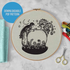 May include: An embroidery hoop with a black and white design of a woman, moon, stars, and a rose tree. The text "DOWNLOADABLE PDF PATTERN" is in a blue circle. Embroidery threads and gold scissors are visible.