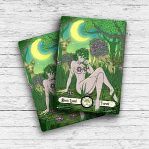 May include: Two fantasy art cards featuring a nude woman with a floral crown and chest covering, sitting in a forest scene with deer and a crescent moon. The cards are labeled "Basic Land" and "Forest".
