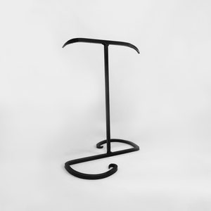 May include: Black metal headphone stand with a curved base and a single horizontal bar for holding headphones.