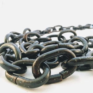 Puede incluir: Primer plano de una cadena de metal negro. La cadena est&aacute; hecha de eslabones gruesos e interconectados. La cadena est&aacute; sobre una superficie blanca.