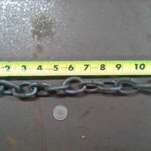 Puede incluir: Primer plano de una cadena plateada que mide 25,4 cm de largo. La cadena est&aacute; sobre una superficie gris con una cinta m&eacute;trica amarilla a su lado.