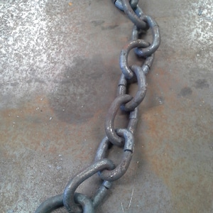 Puede incluir: Primer plano de una cadena plateada con un eslab&oacute;n grande y redondo en el extremo. La cadena est&aacute; sobre una superficie gris texturizada.