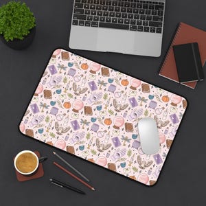 May include: A rectangular desk mat featuring a repeating pattern on a light pink background. The design includes illustrations of owls, crystal balls, purple cauldrons, candles, tarot cards, dragonflies, books, envelopes, and hands with eyes.