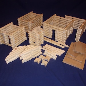 May include: A set of wooden log cabin building blocks, including walls, roof pieces, and a chimney. The blocks are made of natural wood and are ready to be assembled into a log cabin.