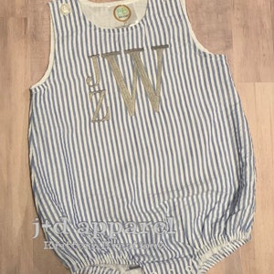 May include: A blue and white striped baby onesie with a silver embroidered monogram "JW".
