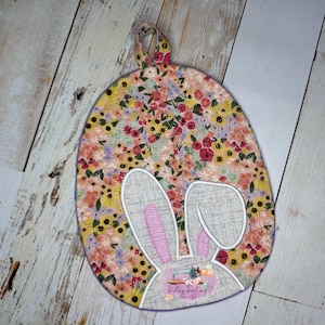 May include: A floral print pot holder with a bunny rabbit design. The bunny has pink ears and a white face. The pot holder has a loop for hanging.