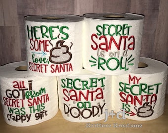 May include: Four rolls of toilet paper with humorous Secret Santa themed embroidery. The rolls feature phrases like "Secret Santa is on a roll", "Secret Santa on Doody", "All I got from Secret Santa was this crappy gift", and "Here's some love, Secret Santa".