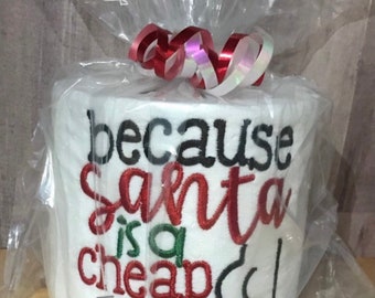 May include: A white toilet paper roll with red and black embroidery that reads "because santa is a cheap [arrow pointing right]"  The roll is wrapped in clear plastic with a red and white ribbon.