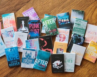 May include: A collection of 20 paperback books with various titles and authors. The books are arranged in a semi-circle on a wooden surface. The books are all different colors and have different designs on their covers.