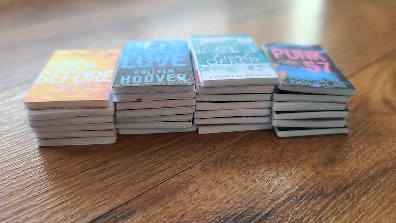 May include: A stack of paperback books with different covers. The covers feature various colors and designs, including a yellow cover with the word "BEFORE" on it, a blue cover with the words "It Ends With Us" and "Colleen Hoover" on it, a green cover with the words "Deal Offer" and "Lauren Asher" on it, and a pink cover with the words "Punk 57" and "Brooke Douglas" on it.