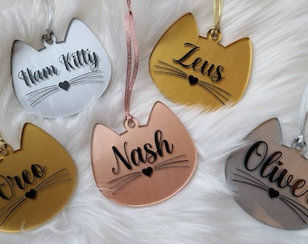 Puede incluir: Cinco adornos con forma de gato con diferentes nombres. Los adornos están hechos de acrílico y vienen en plata, oro, oro rosa y gris claro. Los nombres en los adornos son Ham Kitty, Zeus, Nash, Oreo y Oliver.
