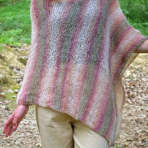 May include: A hand-knitted poncho in a striped pattern of pink, beige, and gray. The open weave garment has a relaxed fit and drapes over the shoulders. The poncho is a cozy, stylish accessory.