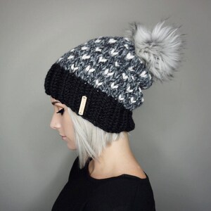 May include: A black and white knit beanie with a fluffy pom pom on top. The beanie has a black band around the bottom.
