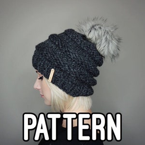 May include: A gray knitted beanie with a fluffy white pom pom on top. The beanie has a cable knit pattern and a small brown leather tag attached to the side. The word "PATTERN" is written in white letters on a black background below the beanie.