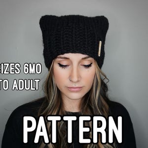 May include: A black knitted beanie hat with a fold-over brim. The hat is shown on a person with long brown hair. The text "SIZES 6MO TO ADULT PATTERN" is visible in the image.