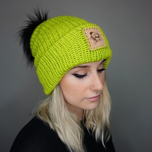 May include: A lime green knit beanie with a black pom pom and a brown leather patch with a skull logo.