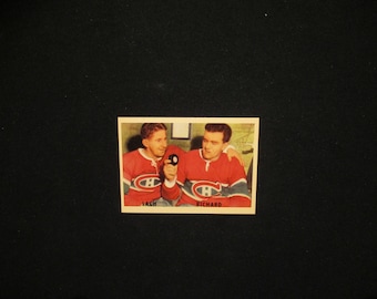 May include: Vintage hockey trading card featuring two men in red jerseys with the Montreal Canadiens logo. The card has the names "Lach" and "Richard" printed on it. The background is black.