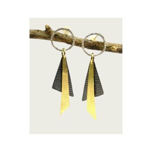 Könnte beinhalten: Ein Paar geometrische Ohrringe mit modernem Design. Jeder Ohrring hat einen strukturierten silberfarbenen Kreis, ein schwarzes Dreieck und ein goldfarbenes, längliches Dreieck. Die Ohrringe hängen an einem goldfarbenen Haken.