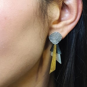 Könnte beinhalten: Silberne und goldene geometrische Ohrhänger mit einer strukturierten silbernen Tropfenform oben und drei geometrischen Formen, die darunter hängen.