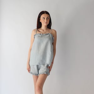 Puede incluir: Un conjunto de pijama de lino azul claro con ribete de volantes. La parte superior es un top sin mangas y los pantalones cortos son de corte holgado.