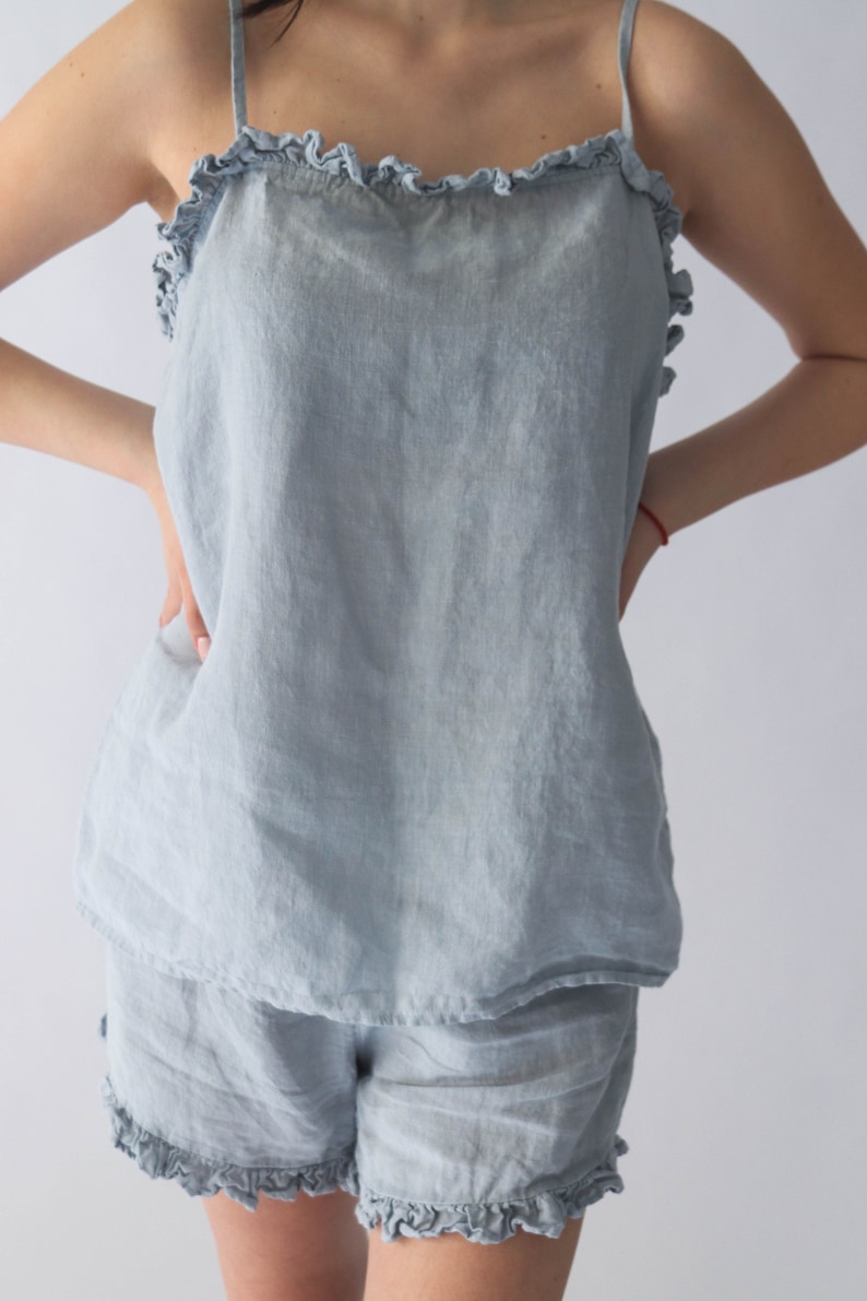Puede incluir: Un conjunto de pijama de lino azul claro con una parte superior y pantalones cortos con volantes.