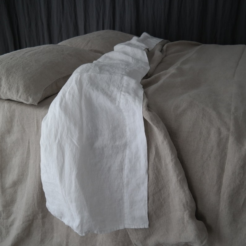 Puede incluir: Un juego de funda n&oacute;rdica de lino beige con un color base beige claro s&oacute;lido y un camino de mesa de lino blanco en contraste drapeado verticalmente por el centro. El juego incluye una funda de almohada beige a juego visible a la izquierda.