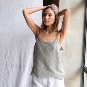 May include: A sleeveless camisole top featuring a vertical grey and white pinstripe pattern with thin shoulder straps and a rounded neckline, paired with solid white shorts that have a relaxed fit and a visible elasticized waistband.