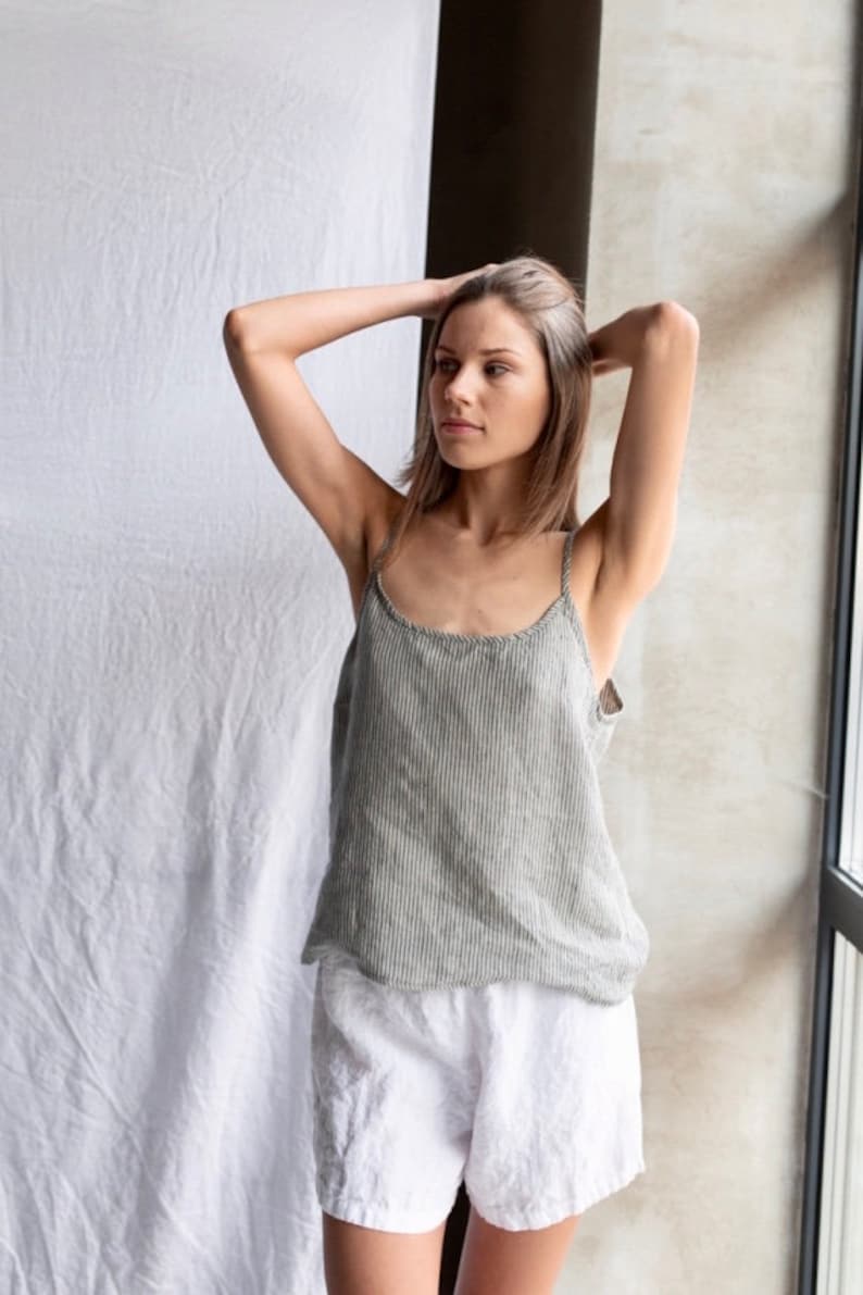 May include: A sleeveless camisole top featuring a vertical grey and white pinstripe pattern with thin shoulder straps and a rounded neckline, paired with solid white shorts that have a relaxed fit and a visible elasticized waistband.