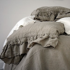 May include: A bed with a beige linen duvet cover and two ruffled pillows. The duvet cover and pillows are made of a soft, natural fabric.