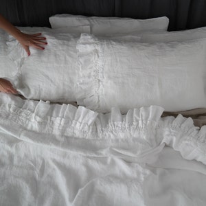 May include: White linen bedding with a ruffled edge. The bedding is made of soft, natural linen and has a relaxed, comfortable look.