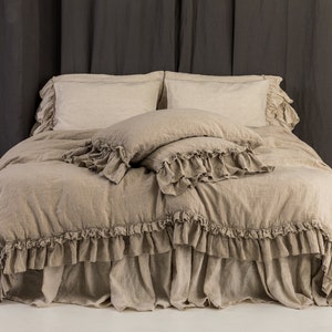 May include: A beige linen duvet cover with a ruffled edge and matching pillowcases. The duvet cover is on a bed with a beige linen bed skirt.
