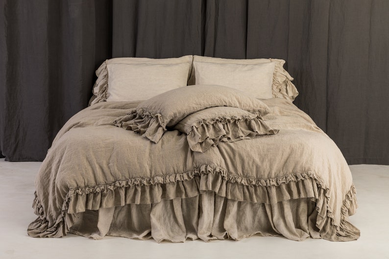 May include: A beige linen duvet cover with a ruffled edge and matching pillowcases. The duvet cover is on a bed with a beige linen bed skirt.
