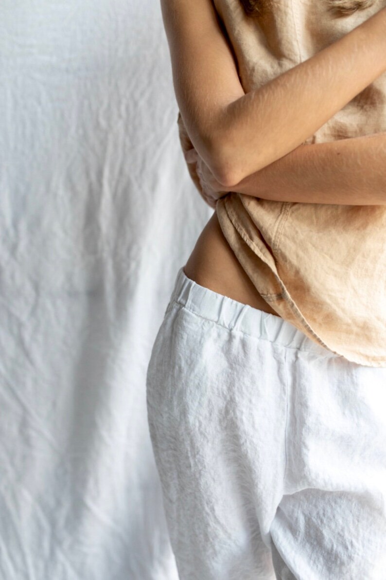 May include: A person wearing white linen pants with a beige linen top. The pants have a drawstring waist and a relaxed fit.