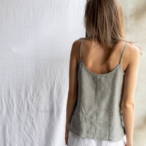 May include: A sleeveless camisole top in a muted sage green color with thin vertical white stripes, featuring a scoop neckline and thin shoulder straps, paired with plain white shorts. The top has a visible vertical seam down the center back.