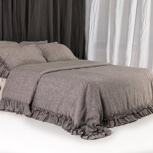 May include: A gray linen duvet cover with a ruffled edge. The duvet cover is on a bed with two pillows and a white bed skirt.