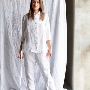 May include: A white linen shirt and pants set with a button-up front and long sleeves. The shirt has a collar and the pants have a relaxed fit.