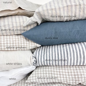 May include: A stack of various linen pillowcases in neutral tones and patterns. The selection includes natural, white, and dusty blue options. Patterns include pinstripes, stripes, and gingham. The text labels each pillowcase with its color or pattern.