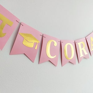 Coquette graduation banner pink and gold.