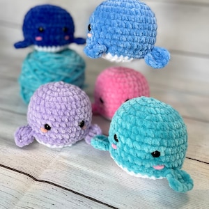 Puede incluir: Cinco peluches de ballena de crochet en diferentes colores: azul, morado, rosa, turquesa y azul claro. Las ballenas tienen vientres blancos y ojos negros.