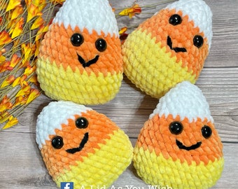 Könnte beinhalten: Vier kuschelige, lächelnde Candy-Corn-Dekorationen. Jedes hat eine weiße Spitze, eine orangefarbene Mitte und einen gelben Boden. Schwarze Knopfaugen und ein aufgestickeltes schwarzes Lächeln vervollständigen das Design. Der Text "A Lid As You Wish" ist enthalten.