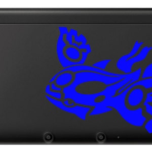Può includere: Una console per videogiochi portatile Nintendo 3DS XL nera con un design di pesce stilizzato blu e bianco sulla cover superiore.