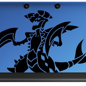 Puede incluir: Una consola de juegos portátil Nintendo 3DS azul con una calcomanía de dragón negro en la tapa superior.