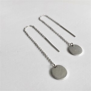 May include: A pair of silver dangle earrings with a small round disc at the end of each chain.