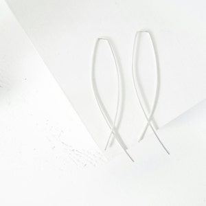 Puede incluir: Un par de pendientes de plata con un diseño simple y curvo. Los pendientes están hechos de alambre fino y tienen un aspecto delicado y minimalista.