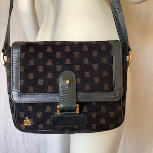 Puede incluir: Bolso de hombro negro con cierre de solapa. El bolso presenta un patrón repetido de formas geométricas marrones en la parte delantera y un logotipo dorado. El bolso tiene una correa verde oscuro y herrajes dorados.