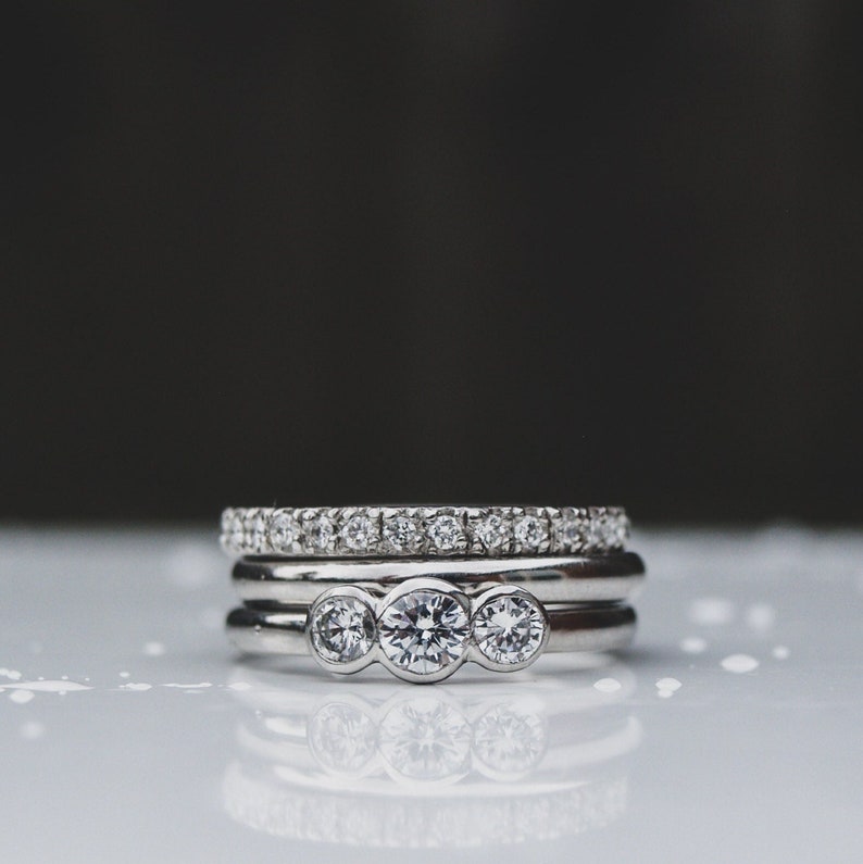 Pode incluir: Tr&ecirc;s an&eacute;is de prata com diamantes. O anel superior tem tr&ecirc;s diamantes grandes no centro. Os dois an&eacute;is inferiores t&ecirc;m diamantes menores engastados numa banda.