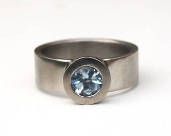 May include: A silver ring with a light blue gemstone set in a bezel setting.