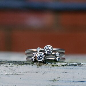 May include: A set of four silver rings with small round diamonds. The rings are stacked on top of each other, with the largest diamond in the center.
