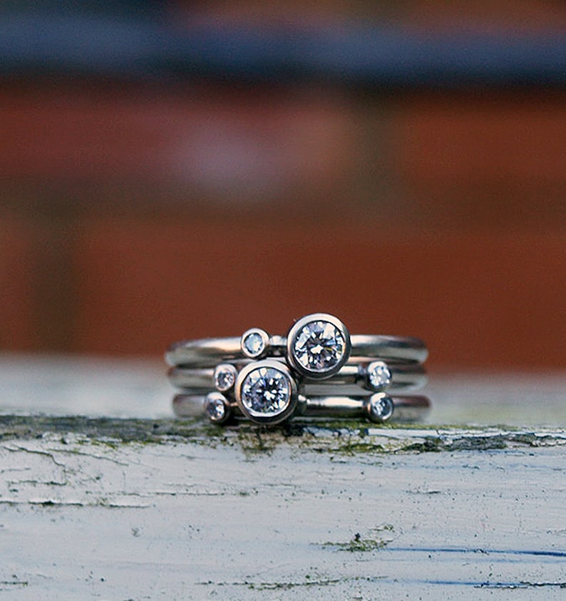 May include: A set of four silver rings with small round diamonds. The rings are stacked on top of each other, with the largest diamond in the center.