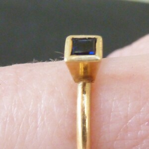 May include: A gold ring with a square-shaped blue gemstone set in a gold setting.